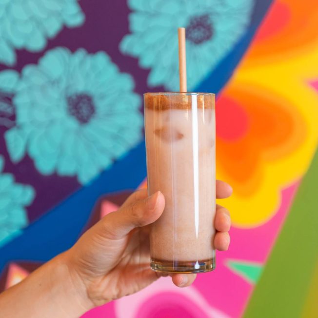 horchata in a tall glass with a straw in front of a colorful mural