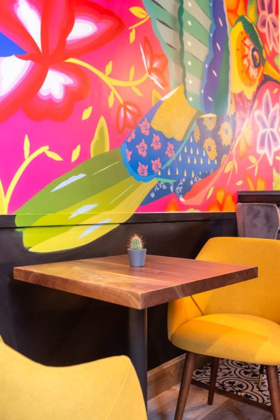 colorful mural and dining table with yellow chairs and cactus